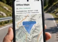 Smartphone displaying a downloaded offline map area held against a scenic mountain road
