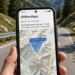 Smartphone displaying a downloaded offline map area held against a scenic mountain road