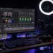 Desktop streaming setup with a monitor showing video production software, ring light and microphone, dark room with LED glow
