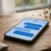 Smartphone on a wooden desk showing a simple blue messaging app with chat bubbles and a small shield icon