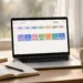 Laptop on a home-office desk showing a colorful weekly content calendar with scheduled social media posts, beside a notebook and a cup of coffee