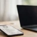 A smartphone showing a generic lock icon beside a laptop on a home desk in soft daylight