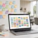 Laptop on a white desk showing a colorful task board with sticky notes on the wall behind
